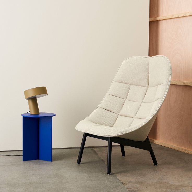 a white chair sitting next to a blue table in front of a wooden shelf with a lamp on it