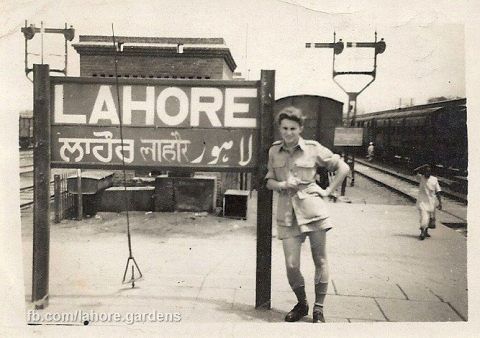 black and white photograph of a woman standing in front of a sign for a train station