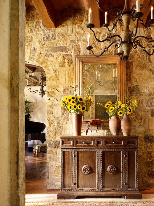 a room with stone walls and a chandelier filled with vases full of sunflowers