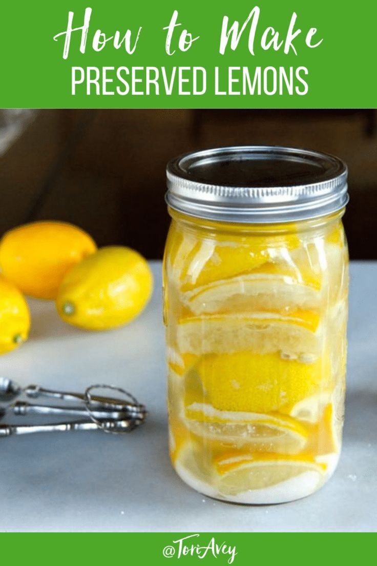 a jar filled with lemons sitting on top of a table next to some fruit