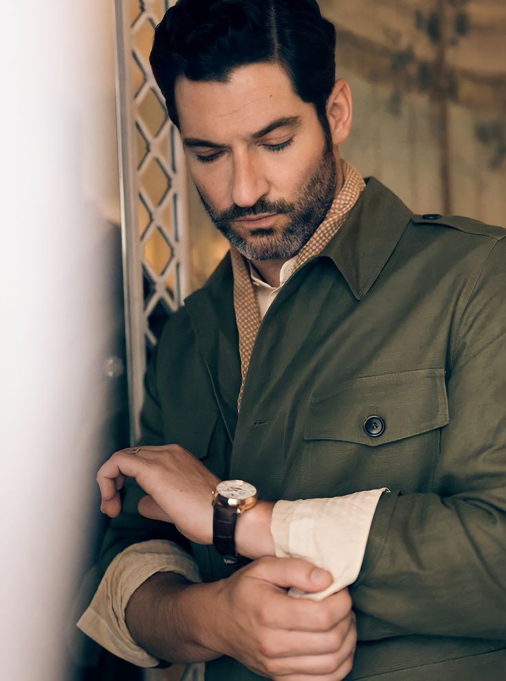 a man with a watch on his left hand is leaning against a wall and looking down