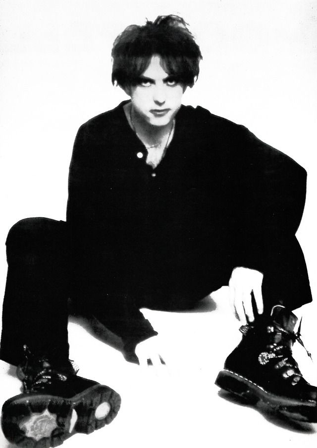 a young man sitting on the ground with his feet up next to two pairs of shoes