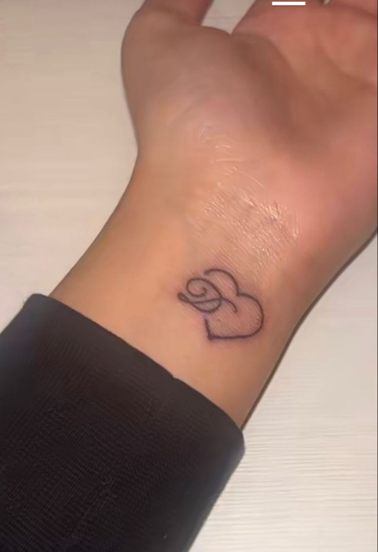 a person's wrist with a small heart tattoo on the left side of their arm