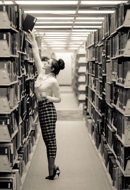 a woman is standing in the middle of a library and reaching up to grab an object