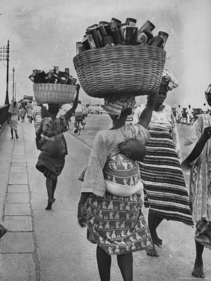 an old black and white photo of women carrying baskets on their heads down the street