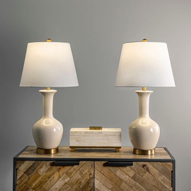 two white lamps sitting on top of a wooden cabinet