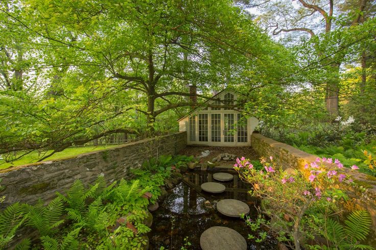 an outdoor pond surrounded by trees and plants with stepping stones in the water next to it