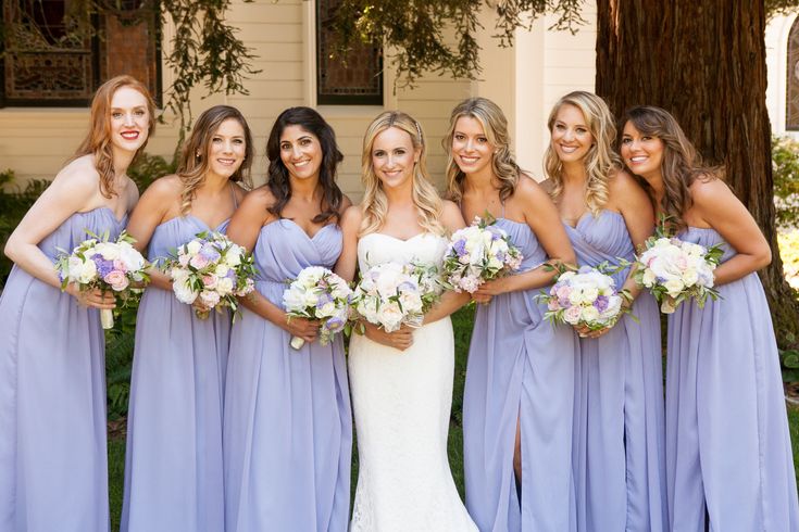 a group of women standing next to each other in front of a house holding bouquets