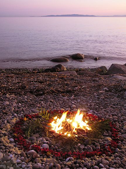 there is a fire pit on the beach with rocks and water in the back ground