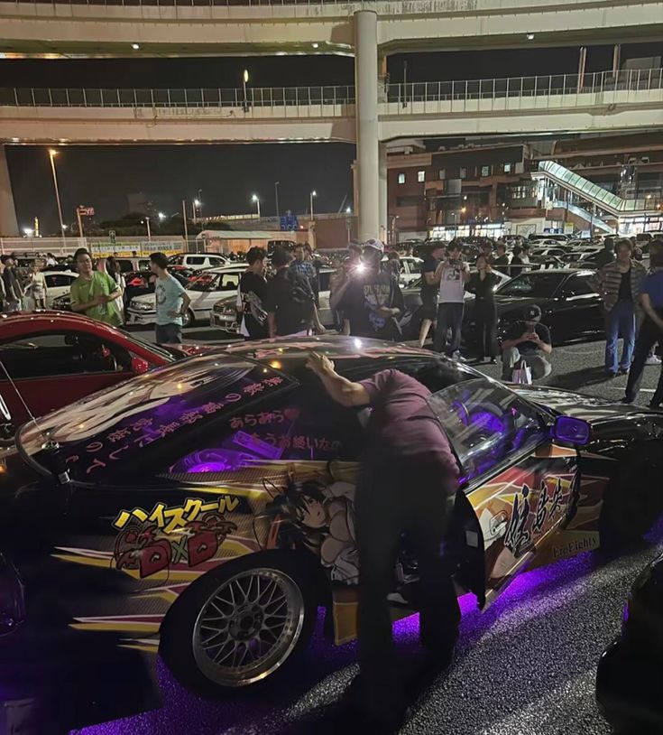 a group of people standing around a parked car in a parking lot next to other cars