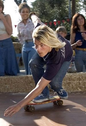 a woman riding a skateboard down the side of a road next to people watching