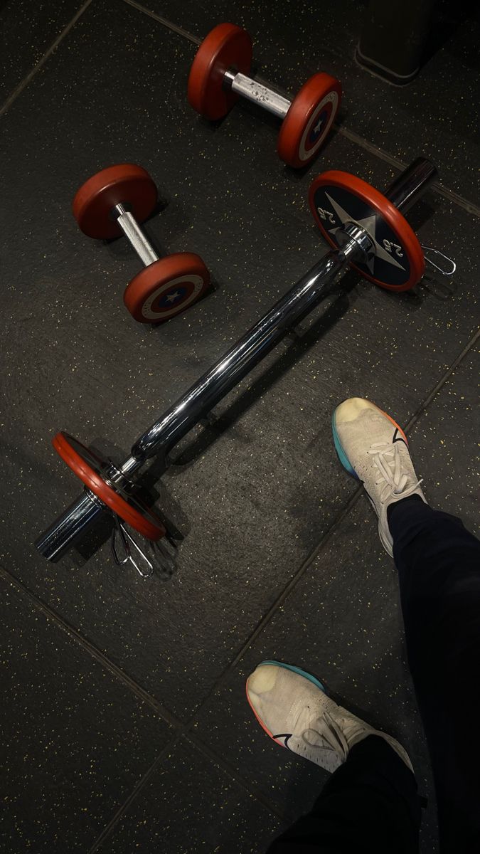 a person standing next to a pair of red dumbbells on top of a floor