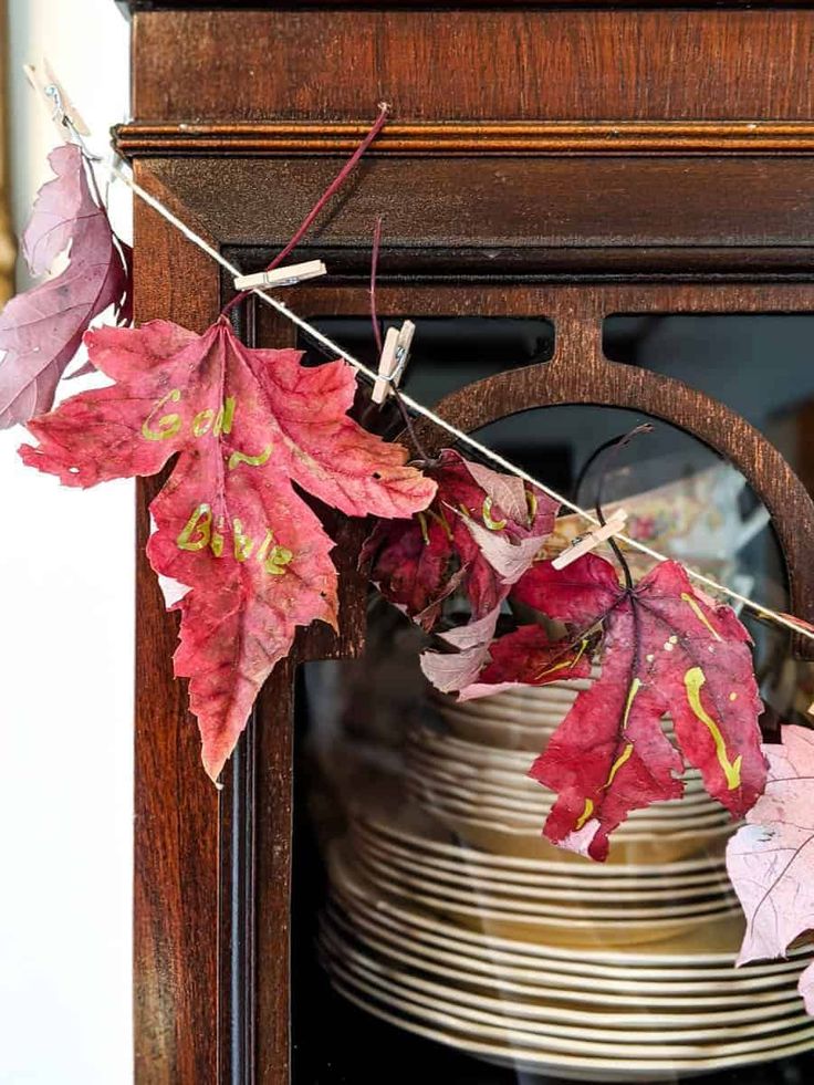 autumn leaves hang from a clothes line on a shelf in front of a china cabinet