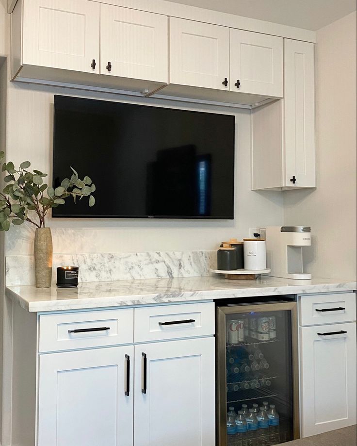 a kitchen with white cabinets and a large flat screen tv above the refrigerator freezer