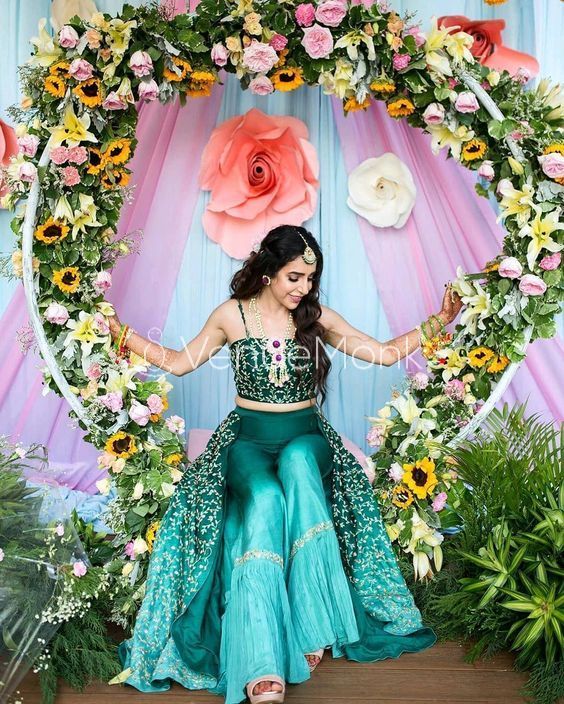 a woman in a green and blue dress sitting on a stage with flowers around her