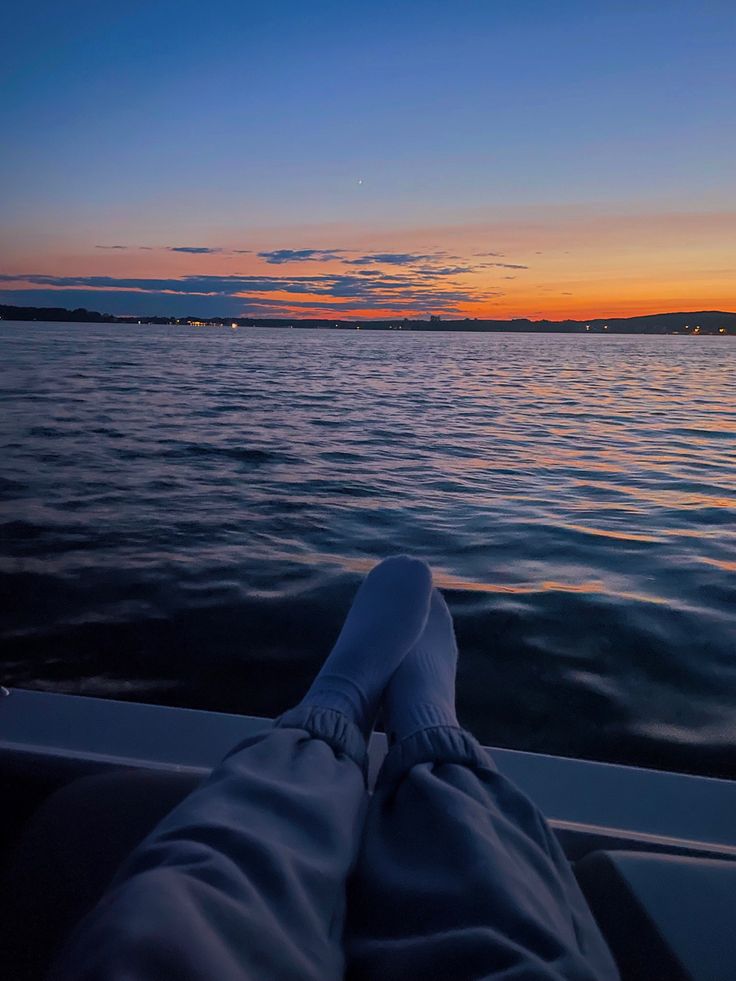 someone is sitting on the back of a boat watching the sun go down over water