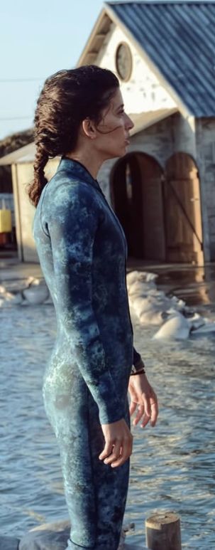 a woman standing on top of a wooden post in the water wearing a wet suit