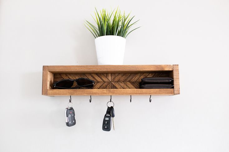 a wooden shelf with keys and sunglasses hanging from it's sides next to a potted plant