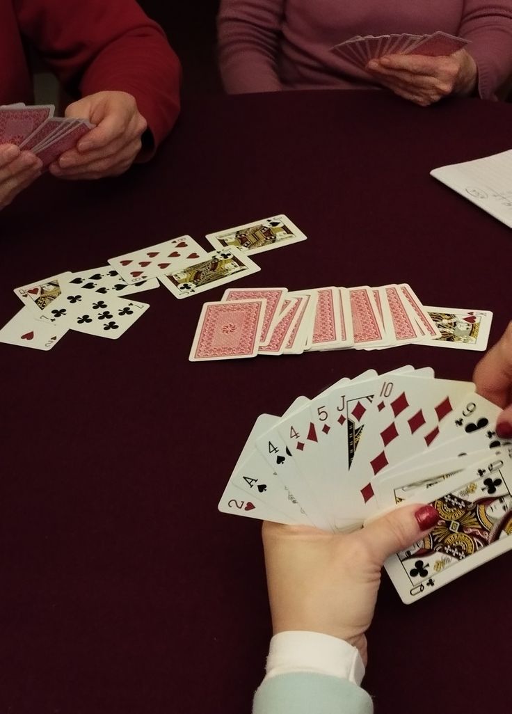 people sitting at a table playing cards with one hand on the other and another holding two