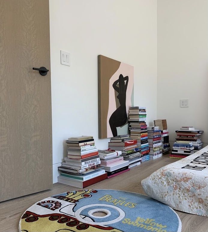 a bed room with a neatly made bed and lots of books on the floor next to it