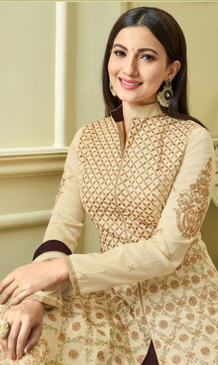 a woman sitting on top of a chair wearing a white and brown dress with intricate designs