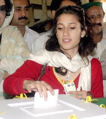 a woman sitting at a table with other people around her looking at something on the table