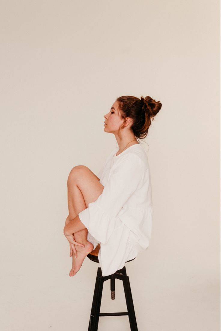 a woman sitting on top of a stool in front of a white wall with her legs crossed