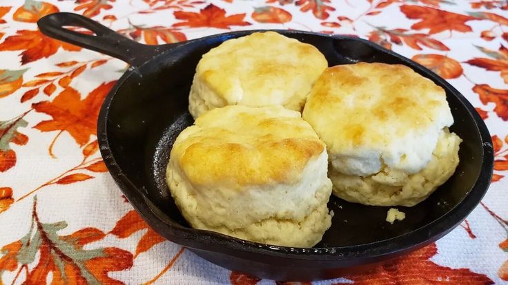 three biscuits in a cast iron skillet on a floral tablecloth with orange flowers