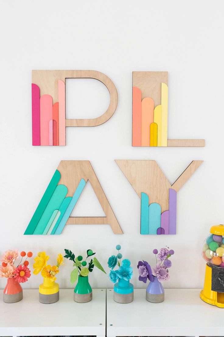 colorful wooden letters and vases on a white shelf next to a wall with flowers