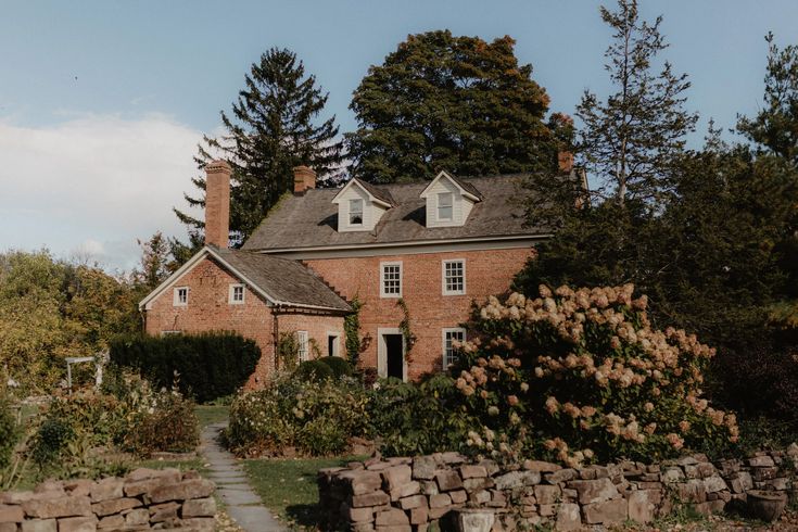 an old brick house surrounded by trees and shrubs with a stone pathway leading to the front door