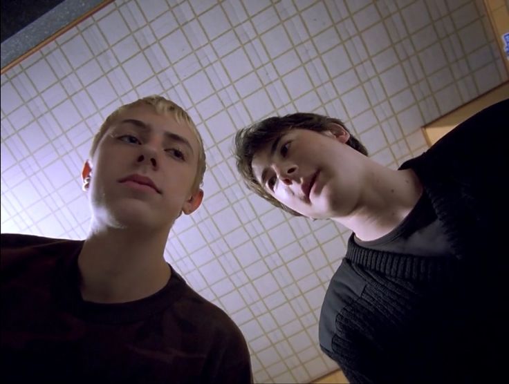 two young men standing next to each other in front of a wall with white tiles