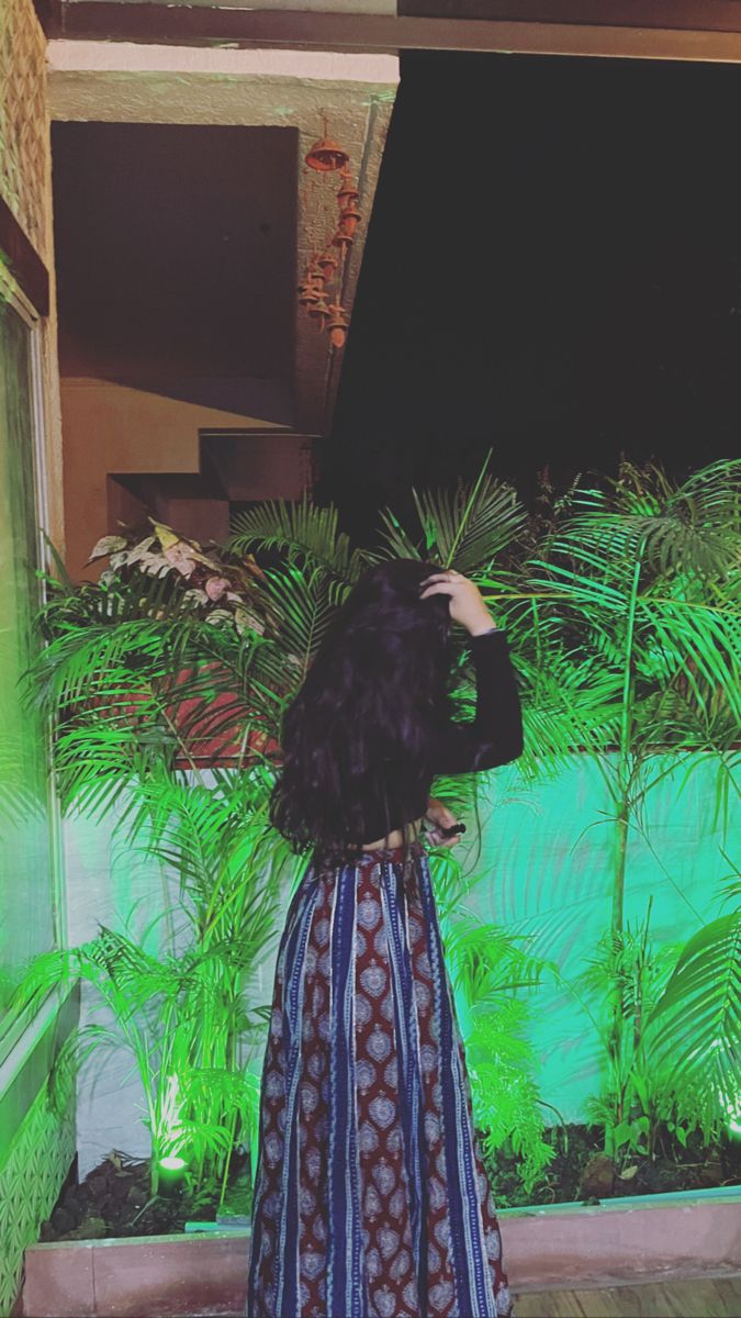 a woman standing in front of a green wall and palm trees with her back to the camera