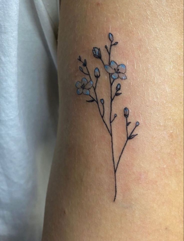 a small flower tattoo on the right side of the arm, with blue flowers growing out of it