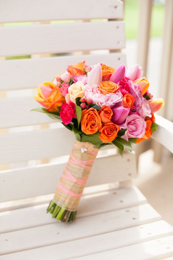 an orange and pink bouquet sitting on top of a white wooden chair in front of a green field