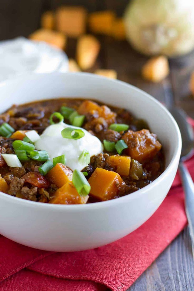 a white bowl filled with chili and meat on top of a red napkin next to a fork