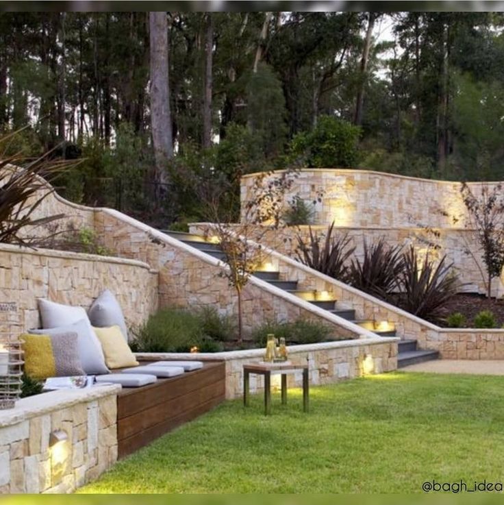 an outdoor living area with stone walls and steps leading up to the top of it