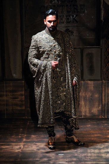 a man standing in front of a wooden floor wearing a black and silver outfit with an elaborate pattern on it