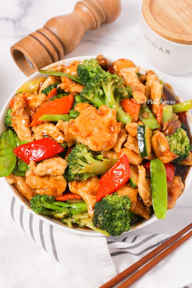 a white bowl filled with chicken and veggies on top of a table next to chopsticks