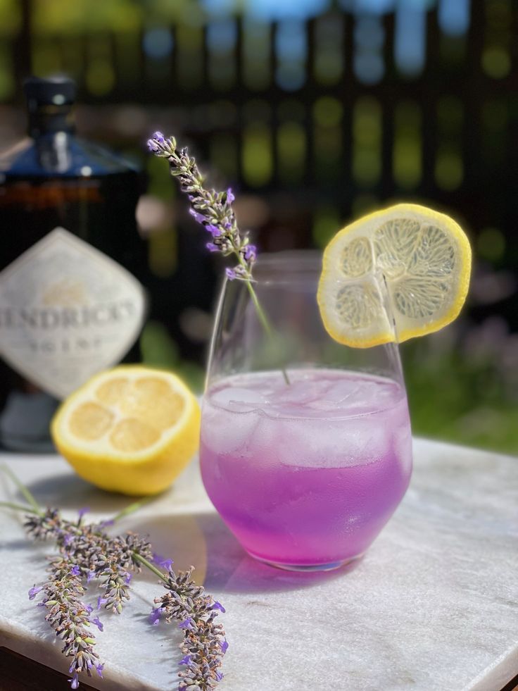 a glass filled with purple liquid next to lemons and lavender