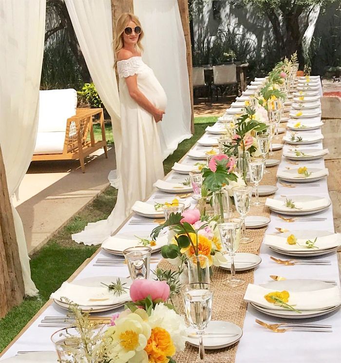 a pregnant woman standing in front of a long table set with plates and glasses on it