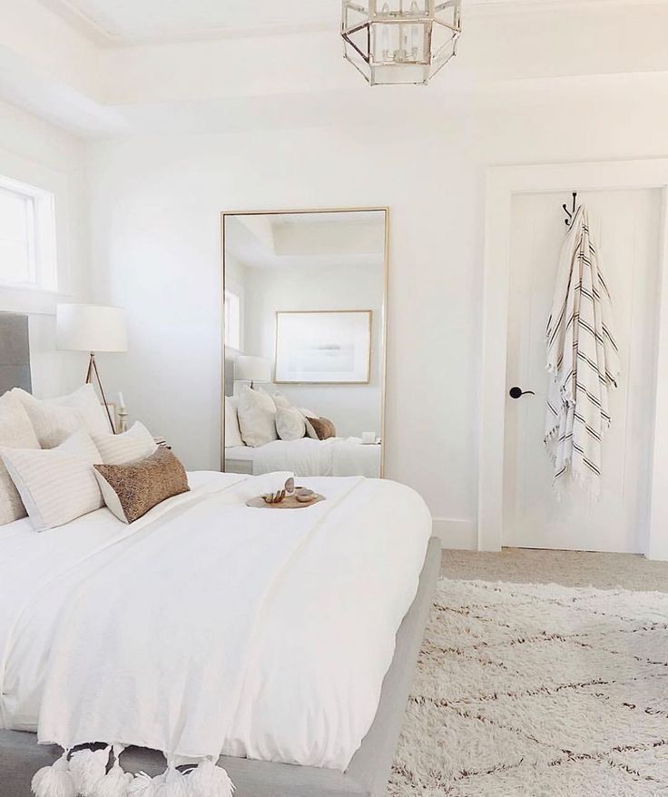 a bedroom with white bedding and pillows in front of a mirror on the wall