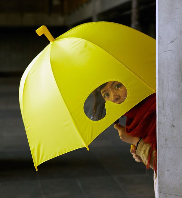 a person with a yellow umbrella looking through the hole in the wall to see what is inside