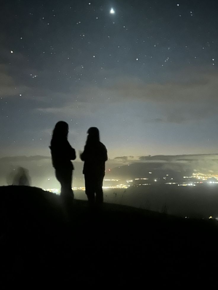 two people standing on top of a hill at night