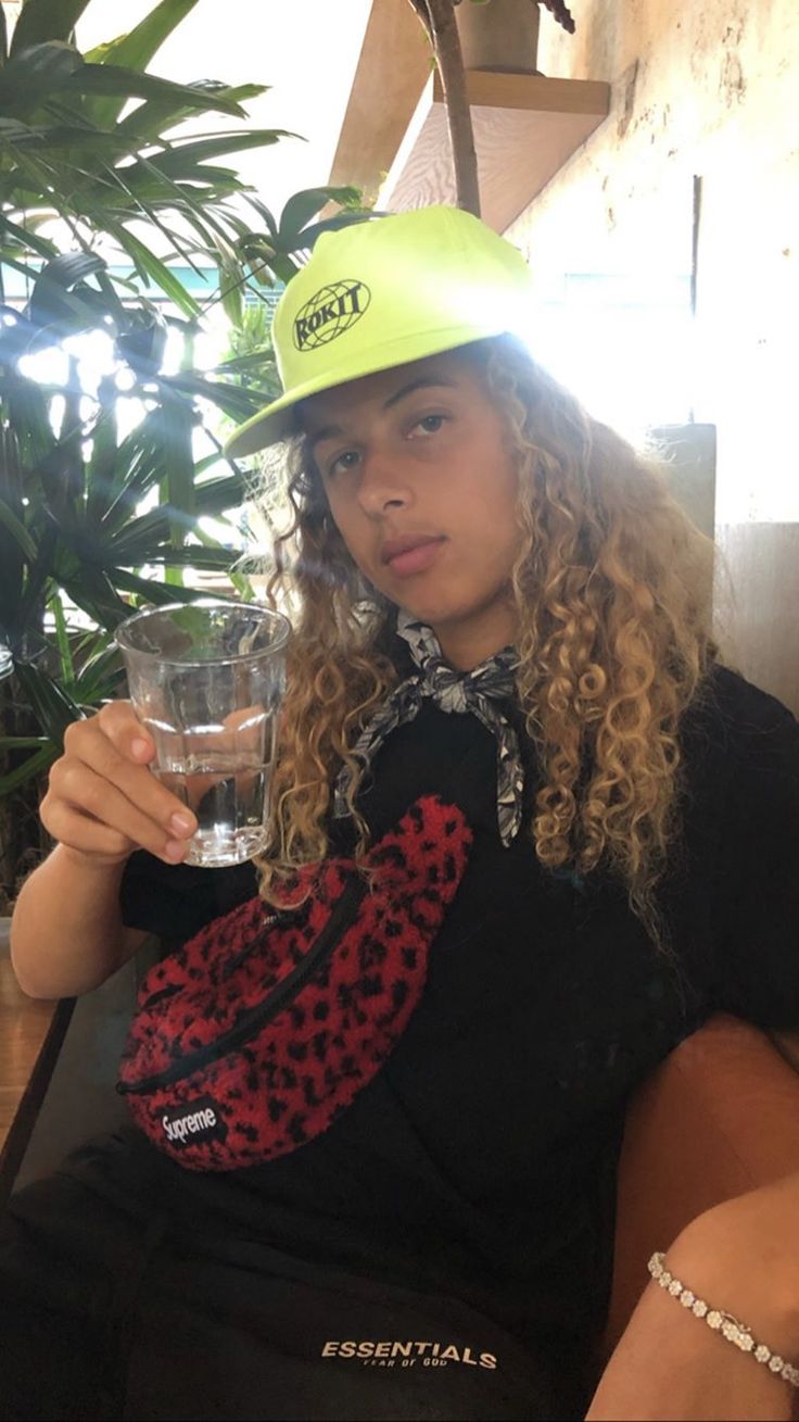 a woman sitting on a couch with a glass in her hand and wearing a green hat