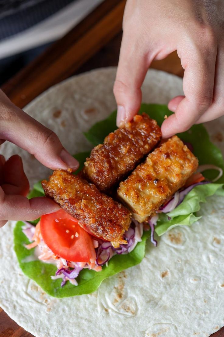 two hands reaching for some food on top of a tortilla with lettuce and tomatoes