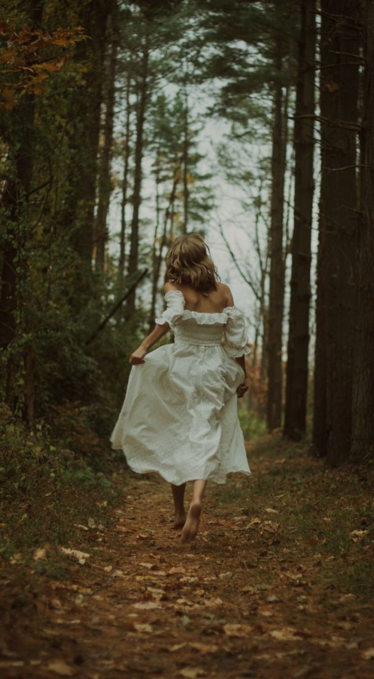 a woman in a white dress is running through the woods