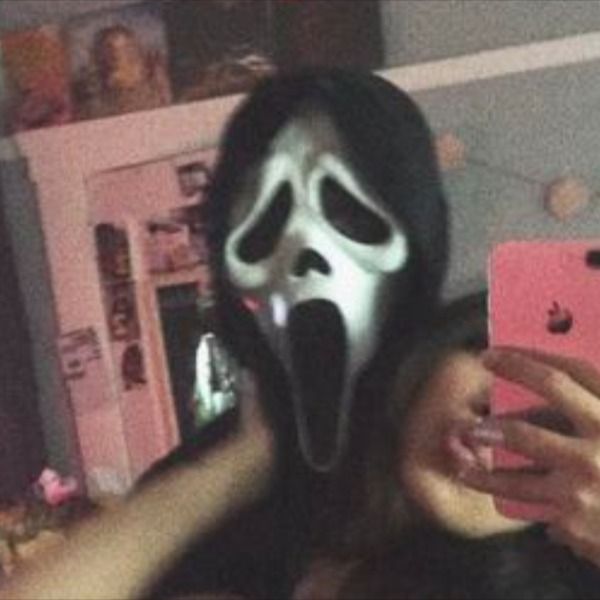 a woman taking a selfie with her cell phone while wearing a ghost face mask