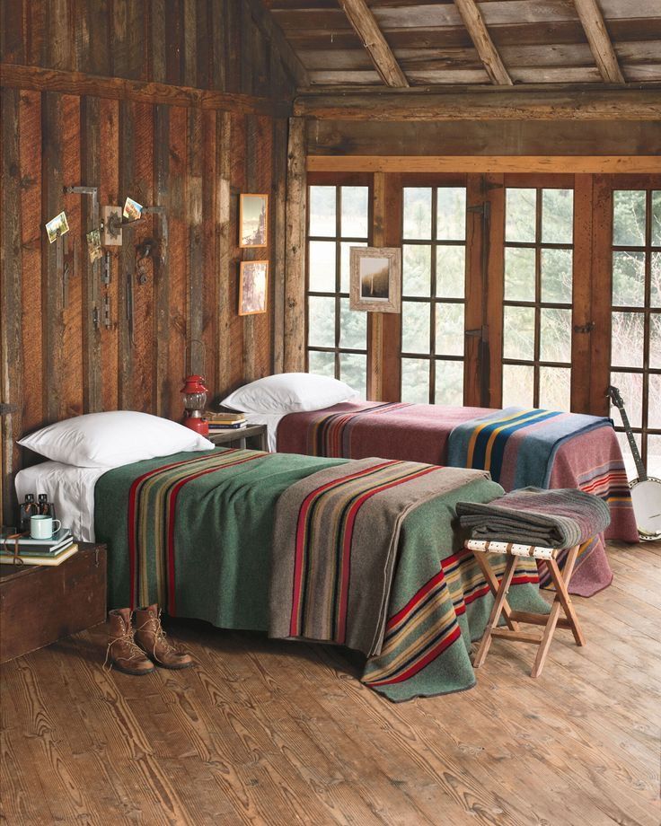 two beds in a room with wooden floors and walls, one has a blanket on the bed