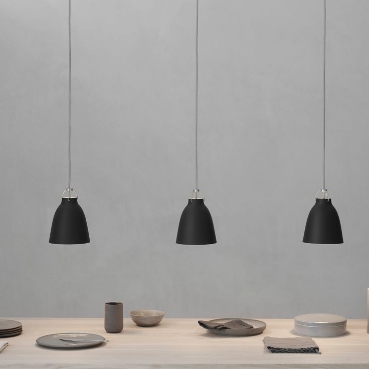 three black lamps hanging from the ceiling above a table with plates and utensils