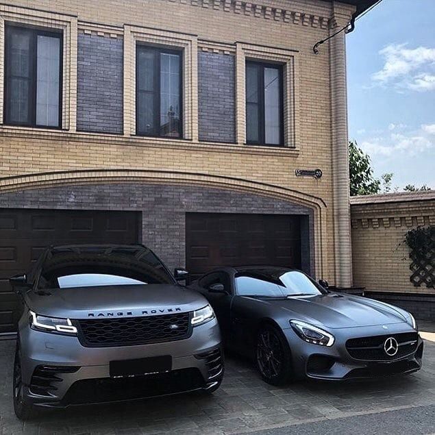 two cars parked next to each other in front of a large brick building with garage doors